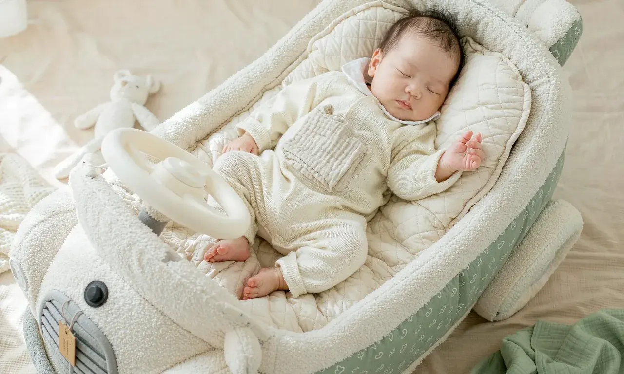 A baby lying on the back inside the quilted basin of the plush convertible car