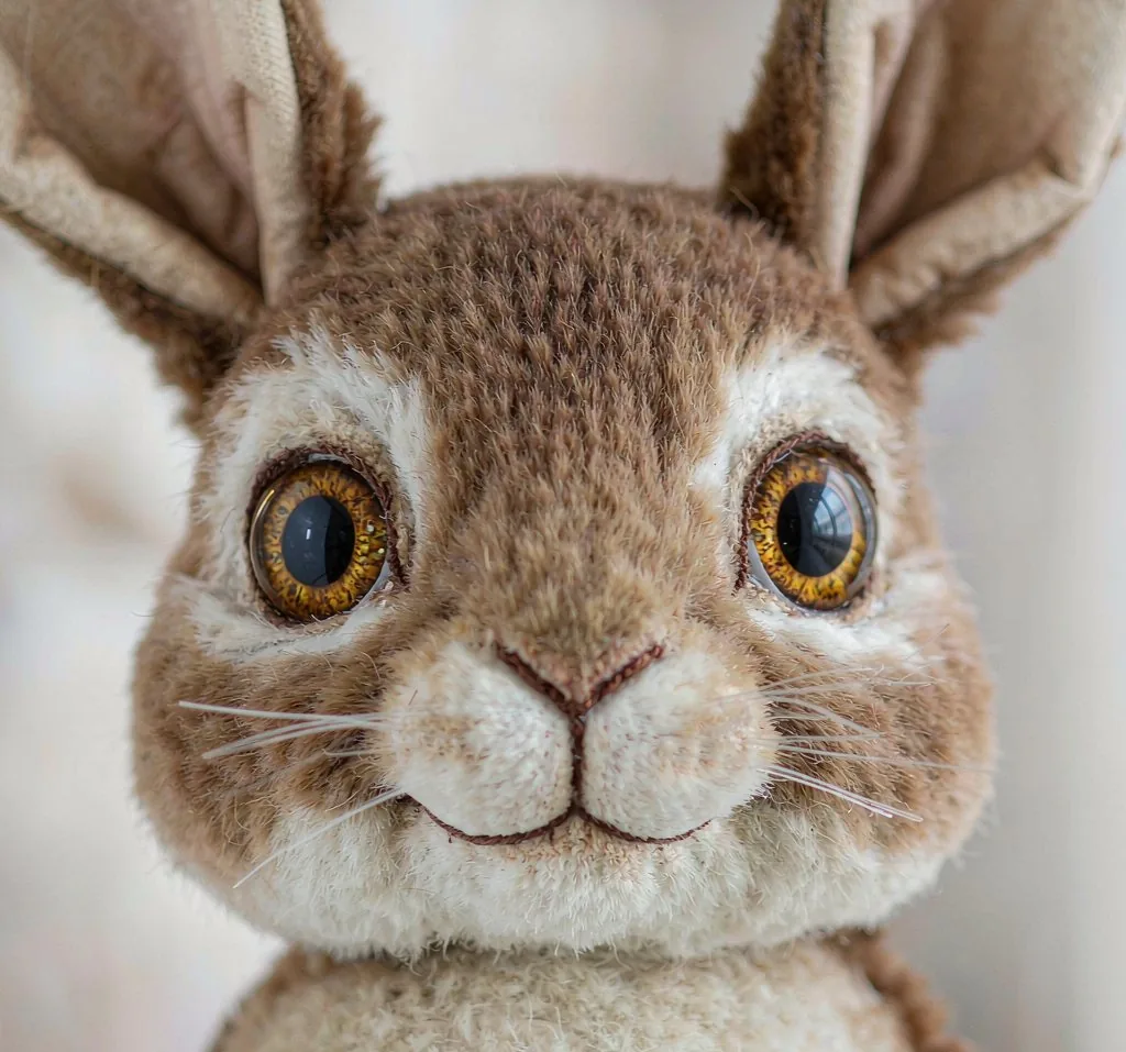 Macro detail of a realistic plush rabbit's glass eye, embroidered nose and trimmed fur
